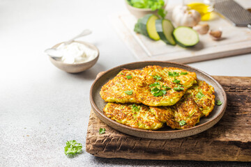 Green zucchini fritters, vegetarian zucchini pancakes with fresh herbs and garlic, served with cream sauce on white background, selective focus