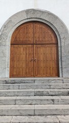 Fototapeta na wymiar A large wide door made of boards, the entrance to the church, a wide staircase made of stone and a white wall