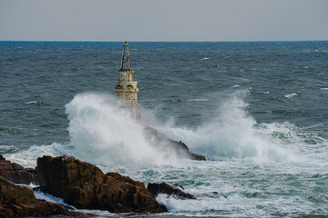 Fototapeta na wymiar Beautiful shot of a water hitting an old lighthouse in the sea and making big powerful splash