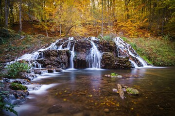 Waterfall dropping from a forest to a river with autumn trees in the background