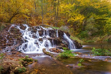 Fototapeta na wymiar Low-angle of Dokuzak waterfall in autumn, yellowing trees background