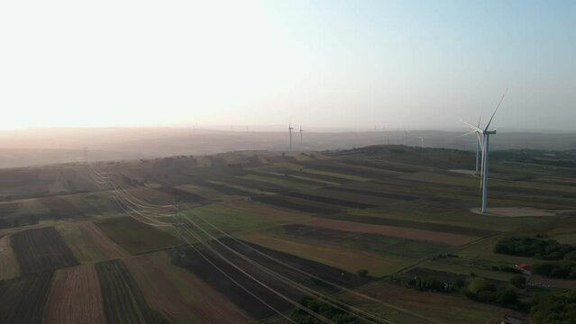 Drone shot over of green fields and windmills against sunrise