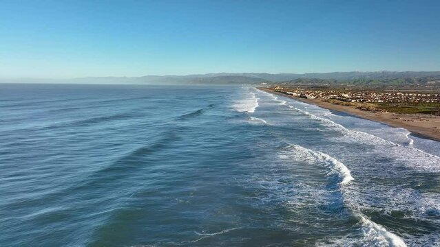 Aerial view of ocean waves crashing against sandy beach with coastal houses in Ventura, California