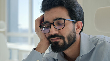 Lazy tired office worker Indian man guy sleepy fatigued bored businessman lean on hand sleep at workplace boring business work low energy burnout depression male drowsy weary exhausted entrepreneur