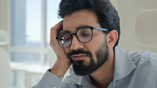 Lazy tired office worker Indian man guy sleepy fatigued bored businessman lean on hand sleep at workplace boring business work low energy burnout depression male drowsy weary exhausted entrepreneur