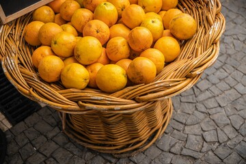Closeup of a  wicker basket filled with ripe oranges resting on a cobblestone pavement