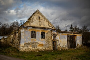 Scenic view of an old rural house with a green lawn and bare trees on a cloudy day