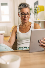 Happy senior woman is reading news on tablet.