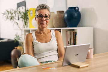 Beautiful old woman with short hair uses tablet and looks at the camera.