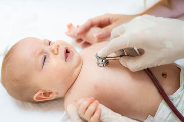 Portrait of crying Caucasian baby during first control examination by pediatrician using stethoscope and medical gloves.