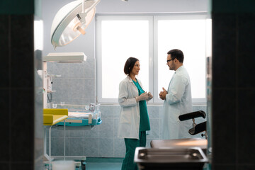 Obraz premium Two serious doctors in uniforms talking face to face with hands in front, while standing in hospital room.