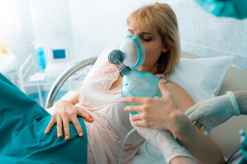 Pregnant woman lying in bed while inhaling nitrous oxide before giving birth to baby. Woman in...