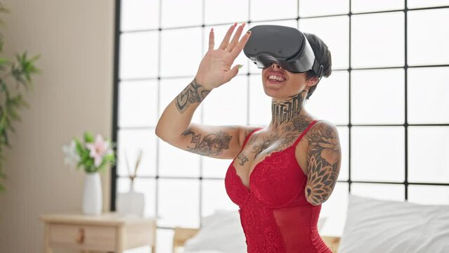 Hispanic woman with amputee arm wearing lingerie sitting on bed using virtual reality glasses at bedroom