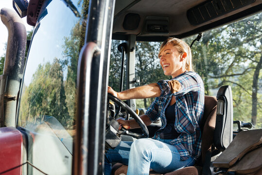 Cheerful farmer driving tractor during harvest at daytime