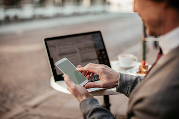 Middle aged caucasian man using a smart phone and laptop in an outdoor cafe