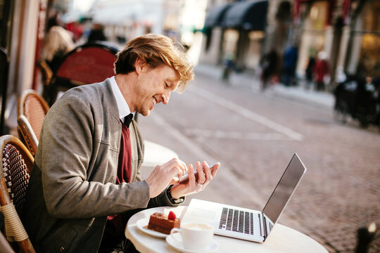 Middle aged caucasian man using a smart phone and laptop in an outdoor cafe