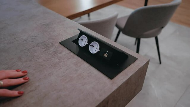 Built-in socket in the kitchen table. A woman opens a built-in socket. Modern interior. Fashionably. Modern device. Elements of modern design.