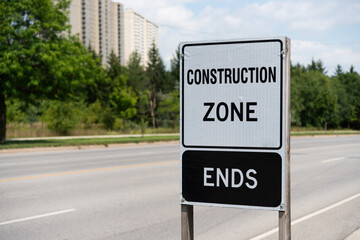 Construction Zone Ends sign with view of road and woodlot and architecture in the distance