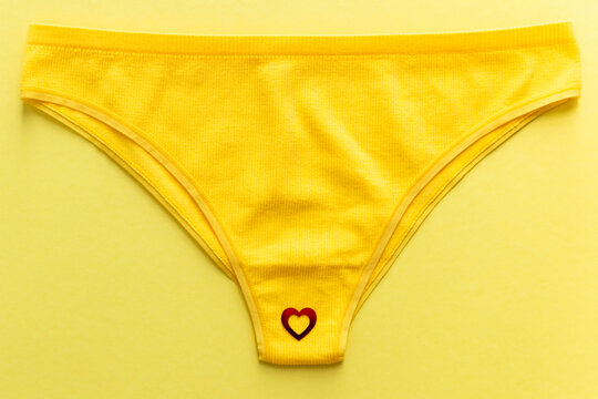 Top view of colorful females panties with red heart confetti on  yellow background