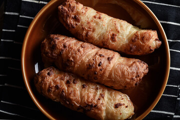 Traditional colombian food, Tequeño or Baked Cheese Stick on a brown plate and black napkin served on a dark table with hot chocolate drink, Dark food lighting