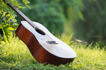 Acoustic guitar outdoors on greenery background. Concept of calm music - obrazy, fototapety, plakaty