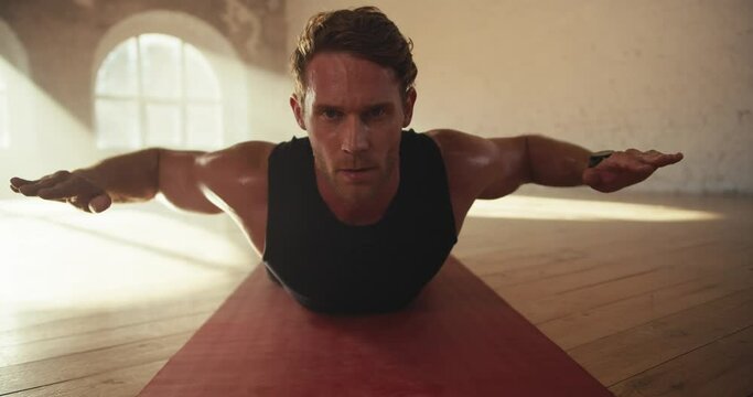 Close-up shot of a male athlete in a black summer sports uniform doing exercises to strengthen the muscles of the back while lying on a special mat in a sunny brick hall