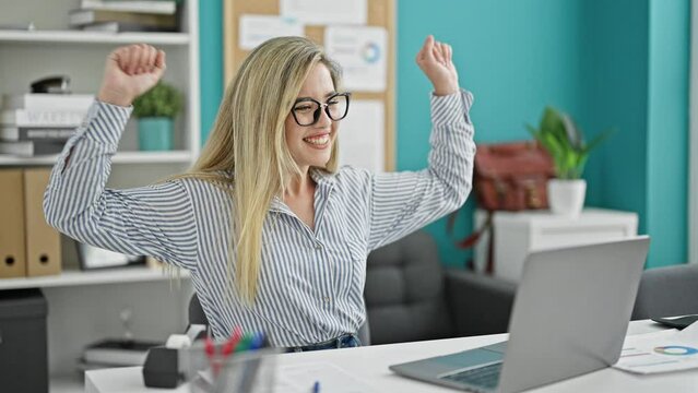 Young blonde woman business worker using laptop working with winner gesture at the office