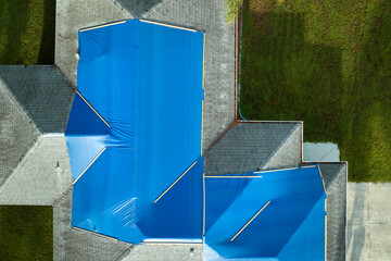Top view of leaking house roof covered with protective tarp sheets against rain water leaks until...