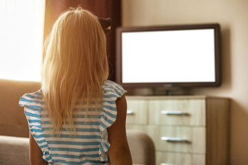 Fototapeta na wymiar Rear view of little girl kid 5-6 year old watching looking tv in living room looking movie. Adorable addiction girl child, empty isolated screen. Television dependency tv concept. Copy ad text space