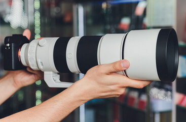 Closeup of a photographer holding onto a camera and large white telephoto lens while wearing.