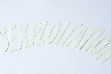 soft-focused word "sexploitation" in light yellow card stock on blank paper