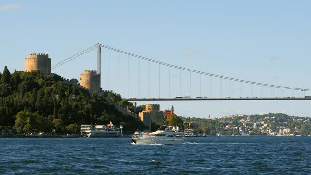 Istanbul Rumeli Hisari Fortress with the Perili Kosk on Bosphorus Sea. Luxury white yacht sails past the historical castle. 4K Cinematic, telephoto shot. Yusuf Ziya Pasha Kiosk, Istanbul, Turkey
