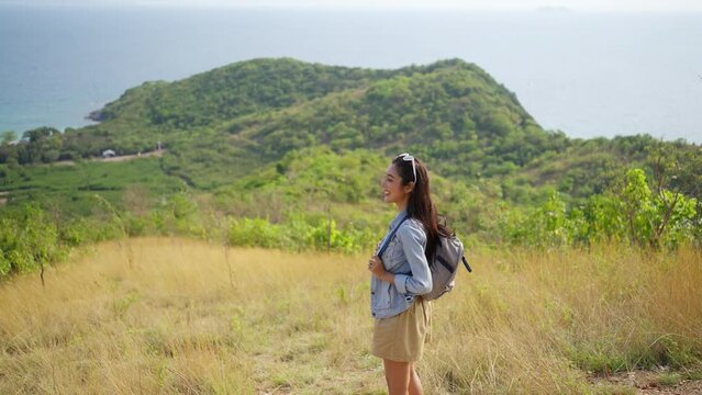 Asian woman walking on mountain peak looking beautiful ocean at tropical island in sunny day. Attractive girl relax and enjoy outdoor lifestyle solo travel nature at the sea on summer holiday vacation
