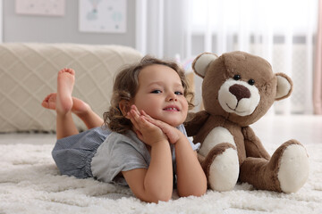 Cute little girl with teddy bear on floor at home