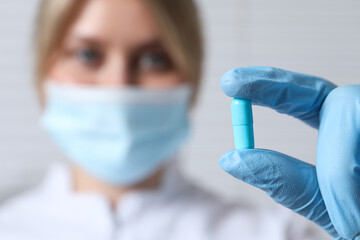 Doctor holding pill on light background, selective focus. Space for text