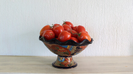 Recipiente de cer&aacute;mica en forma de copa con jitomates rojos en su interior sobre superficie de madera.  