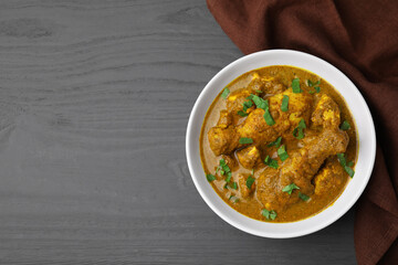 Delicious chicken with curry sauce on grey wooden table, top view. Space for text
