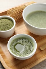 Fresh matcha tea, bamboo whisk and green powder on wooden tray, closeup