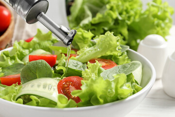Pouring oil into delicious vegetable salad on white table, closeup