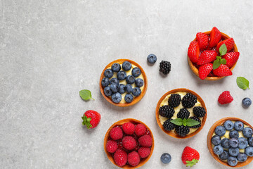 Tartlets with different fresh berries on light grey table, flat lay and space for text. Delicious...