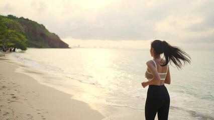 4K Confidence Asian woman in sportswear jogging exercise on tropical island beach in summer morning. Healthy female enjoy outdoor activity lifestyle sport training running workout on beach vacation