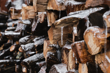 section of firewood stack covered in ice with icicles hanging from them. Aftermath of an icestorm on raw firewood