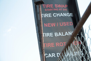 tire swap starting at 40 dollars tire change new used tire balance tire rotation car detailing vertical rectangle sign, fence in front, red and white writing caption text on black background