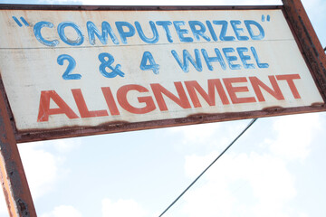 computerized 2 and 4 wheel alignment writing caption text rectangle horizontal sign with sky and cable in background, blue and red writing on white background