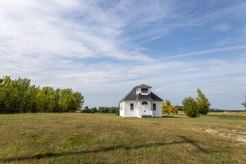 Sunny landscape view of a rural 19th century wood constructed one-room country schoolhouse on a prairie in midwestern USA, with blue sky background.