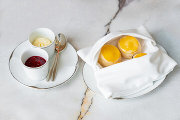 British Scones inside white napkin with clotted cream, and strawberry jam on white marble table