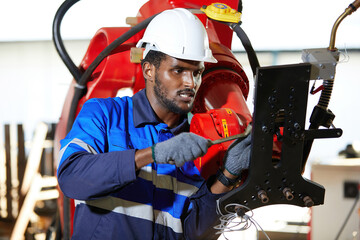 African engineer or worker checking and fixing machine in robot factory