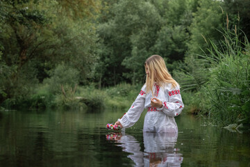 Portrait of a beautiful fair-haired girl in national clothes near a forest river.