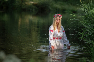 Portrait of a beautiful fair-haired girl in national clothes near a forest river.
