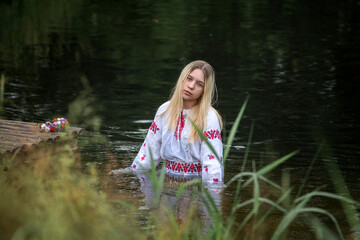 Portrait of a beautiful fair-haired girl in national clothes near a forest river.
